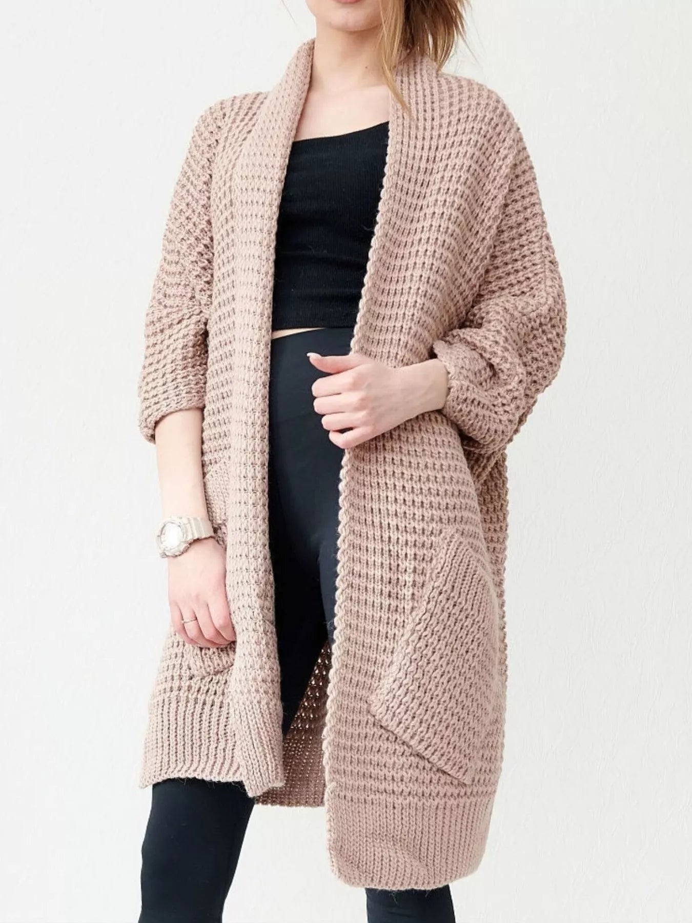 Woman wearing a blush-pink Chunky Knit Open Front Cardigan with a textured waffle weave and deep front pockets, styled over a black top.