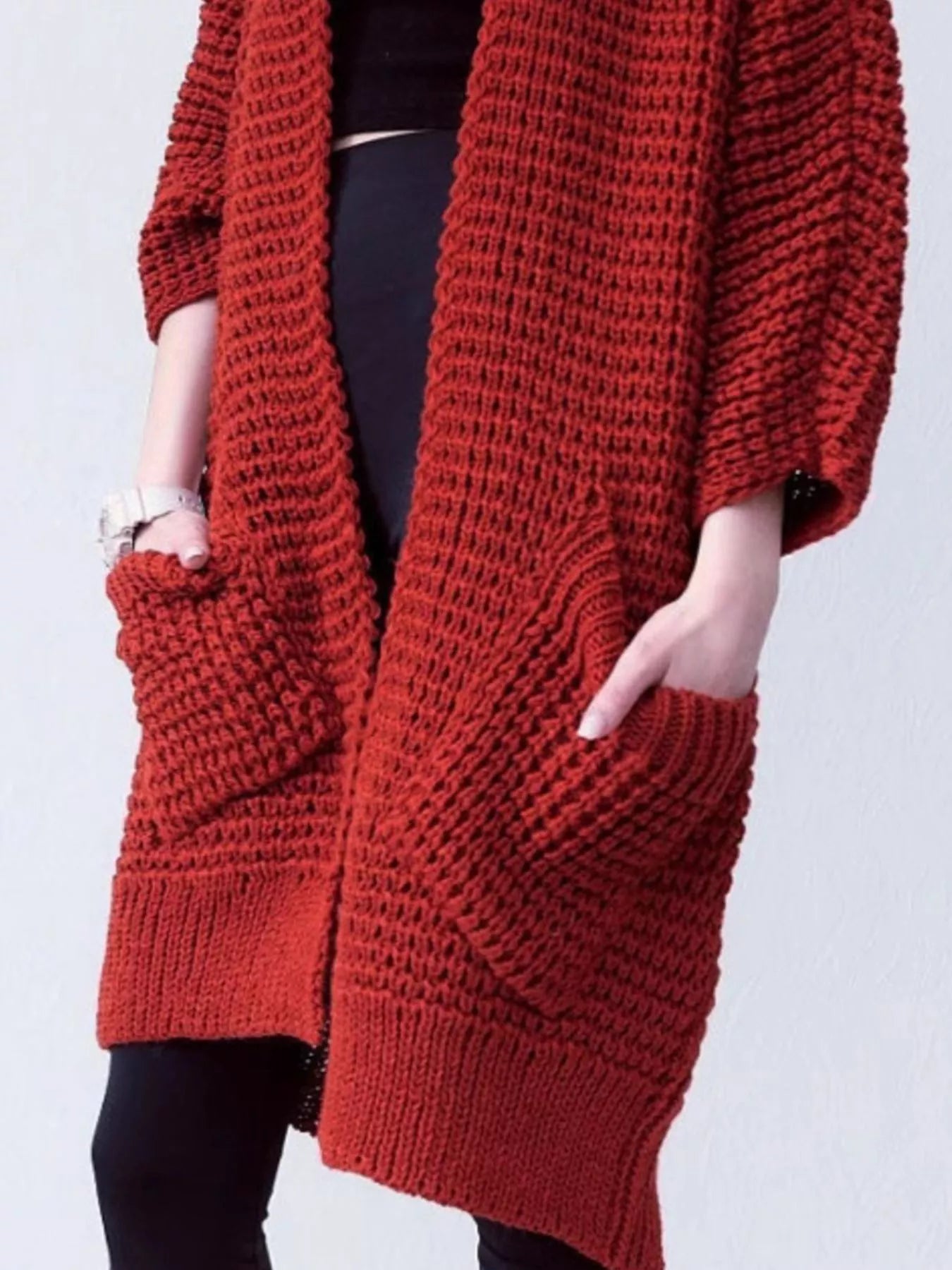 Woman wearing a cozy, rust-red Chunky Knit Open Front Cardigan with a textured waffle weave and deep front pockets, styled over a black outfit.