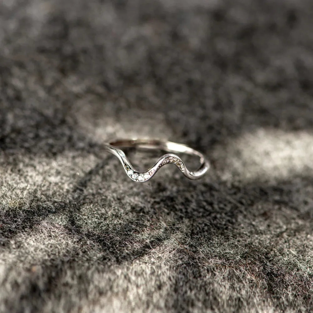 Silver wave-shaped ring on a textured stone surface