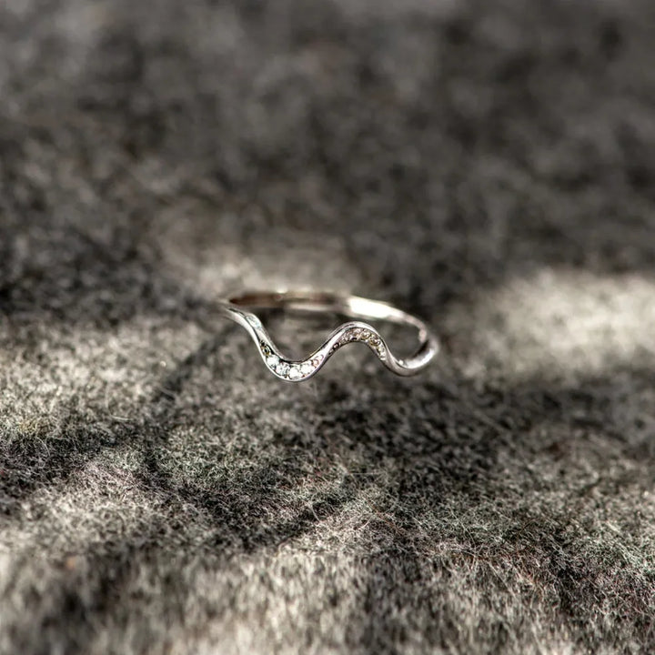 Silver wave-shaped ring on a textured stone surface