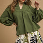 Woman wearing a green blouse and patterned pants against a beige background
