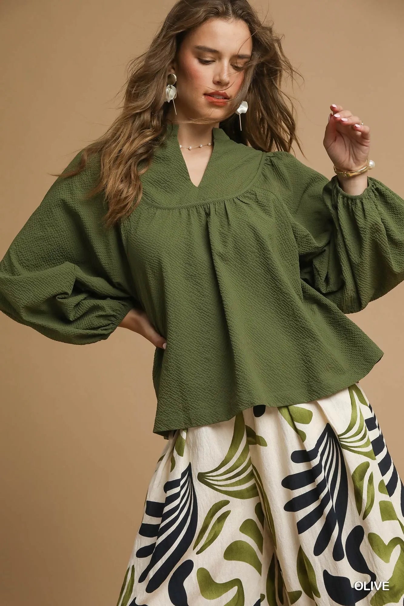 Woman wearing a green blouse and patterned pants against a beige background