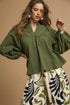 Woman wearing a green blouse and patterned pants against a beige background