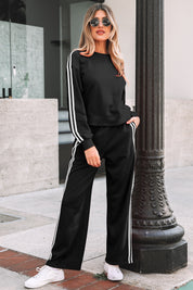Woman wearing a black tracksuit with white stripes standing outdoors.