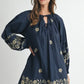 Woman wearing a navy blue dress with floral embroidery on a white background