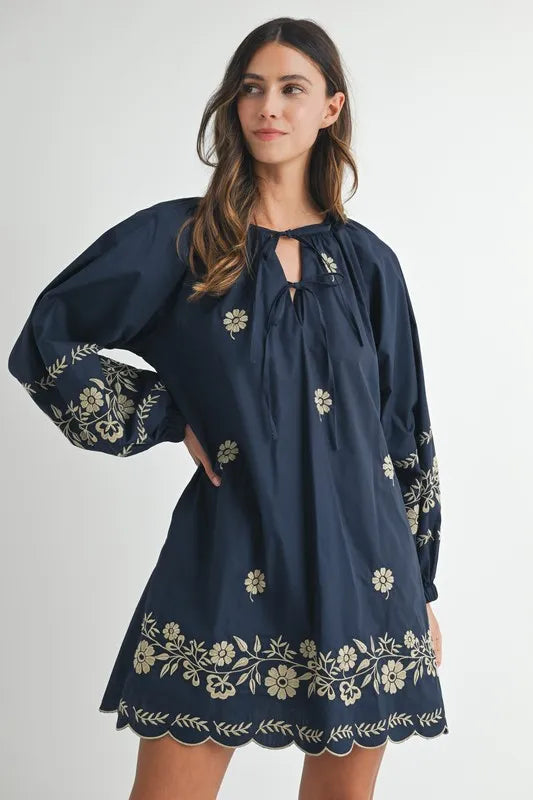 Woman wearing a navy blue dress with floral embroidery on a white background