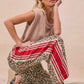 Woman in beige knit sleeveless top and BiBi leopard print pants with red stripes