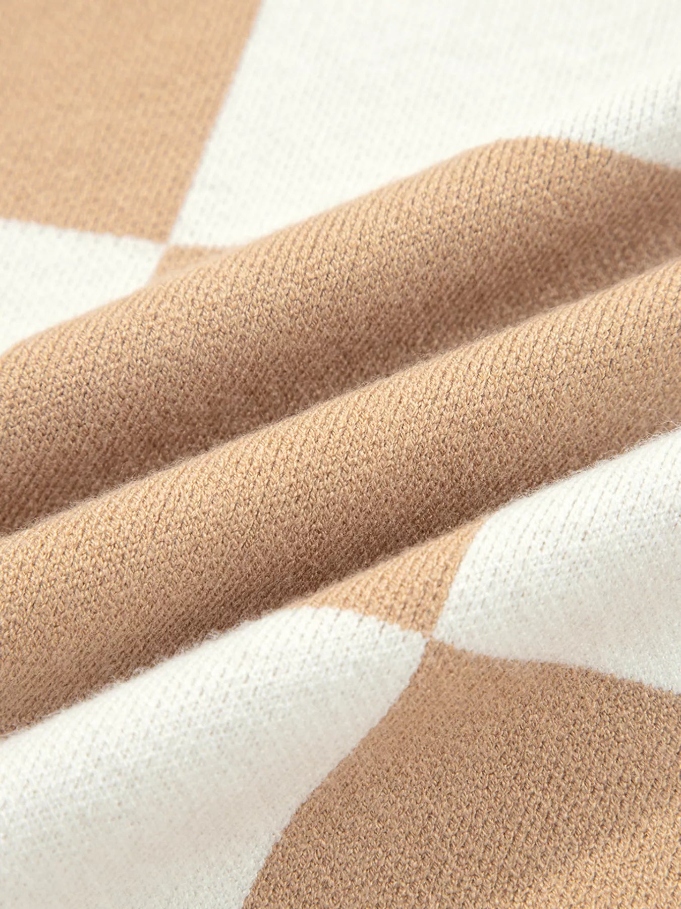 Beige and white geometric knit throw blanket on checkered sweater