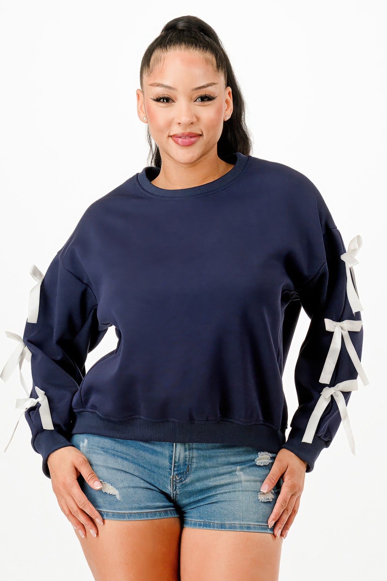 A woman wearing a navy blue crewneck sweatshirt with white bows on sleeves