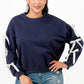 A woman wearing a navy blue crewneck sweatshirt with white bows on sleeves