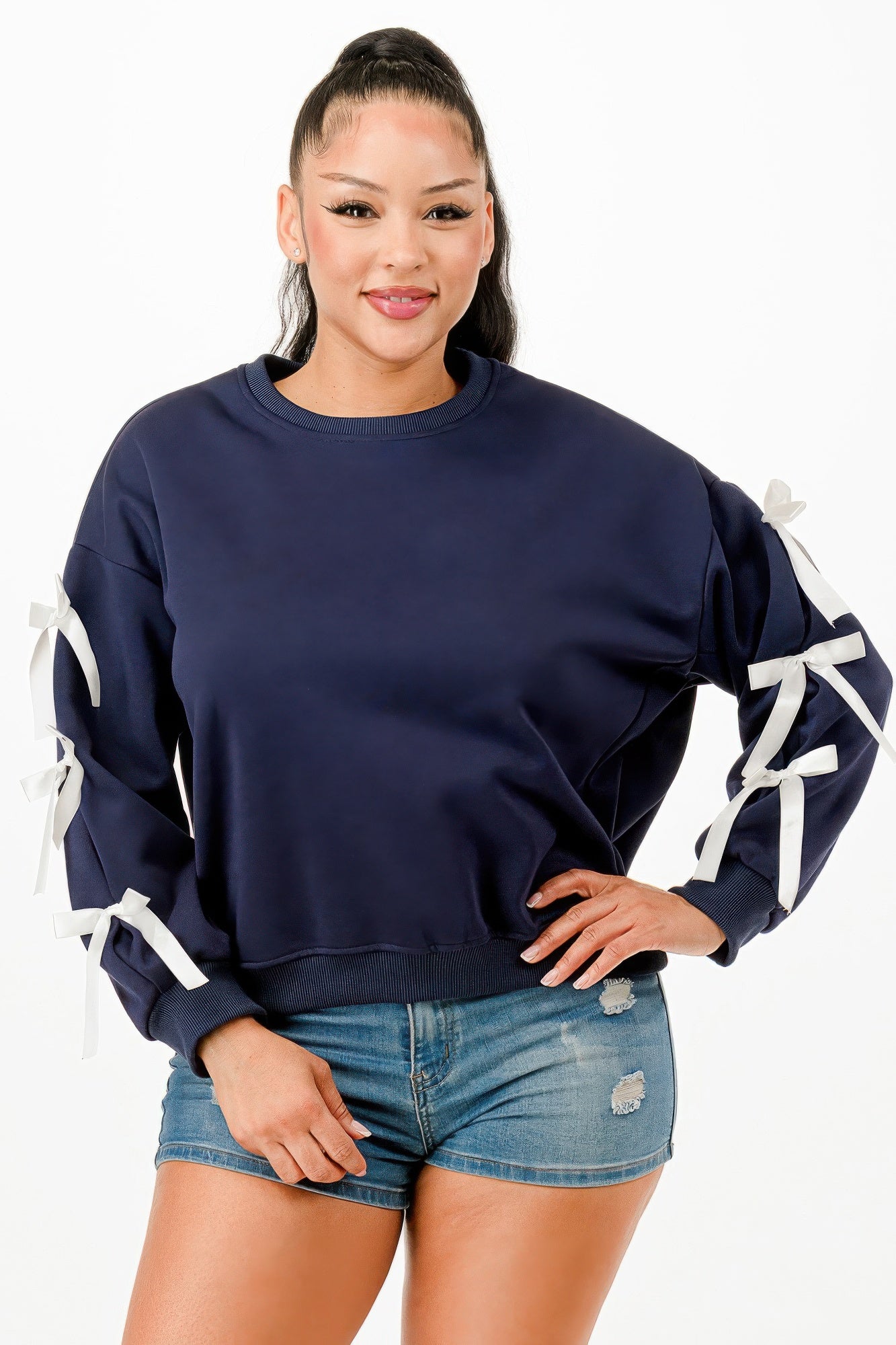 A woman wearing a navy blue crewneck sweatshirt with white bows on sleeves