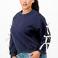 A woman wearing a navy blue crewneck sweatshirt with white bows on sleeves