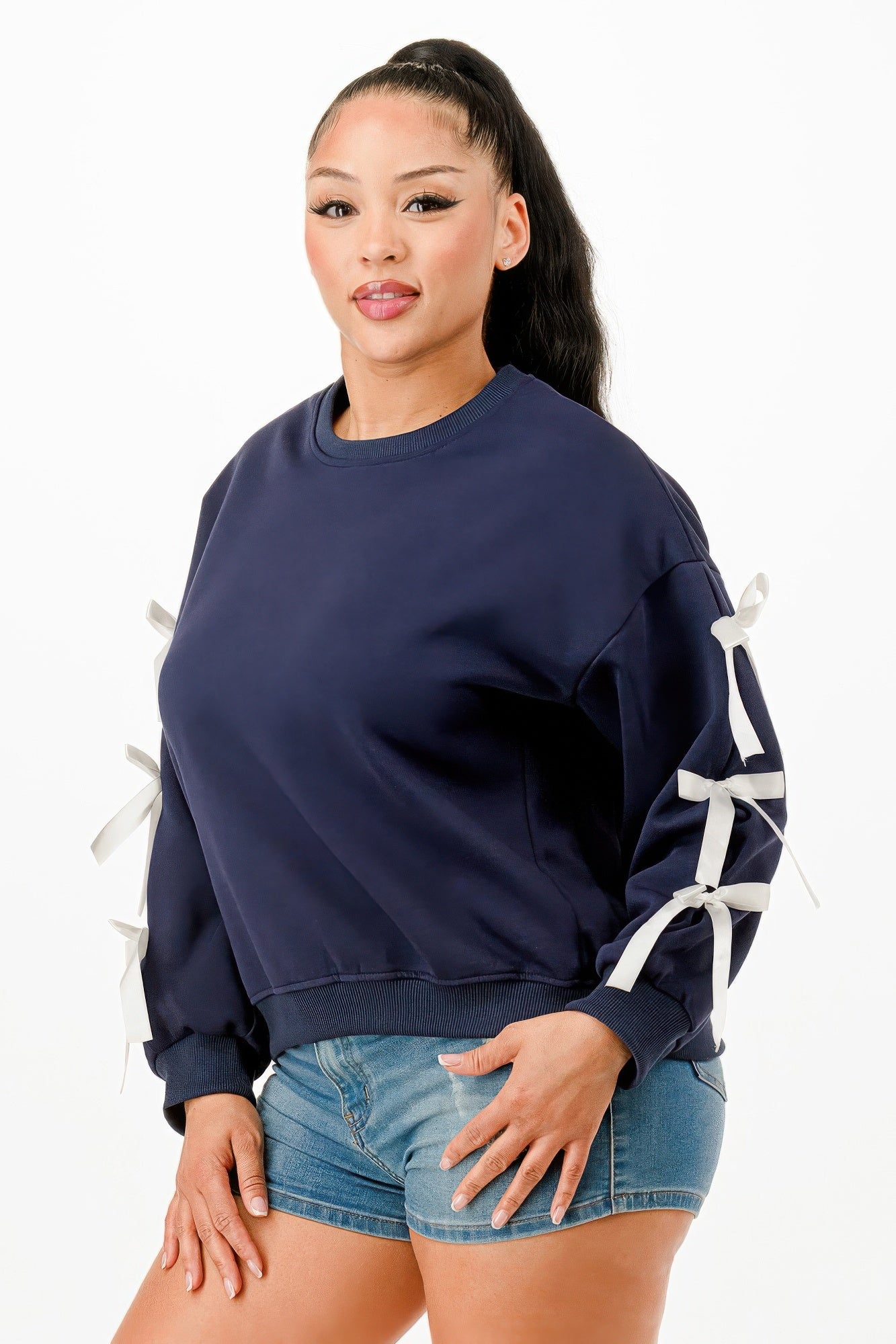 A woman wearing a navy blue crewneck sweatshirt with white bows on sleeves
