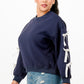 A woman wearing a navy blue crewneck sweatshirt with white bows on sleeves