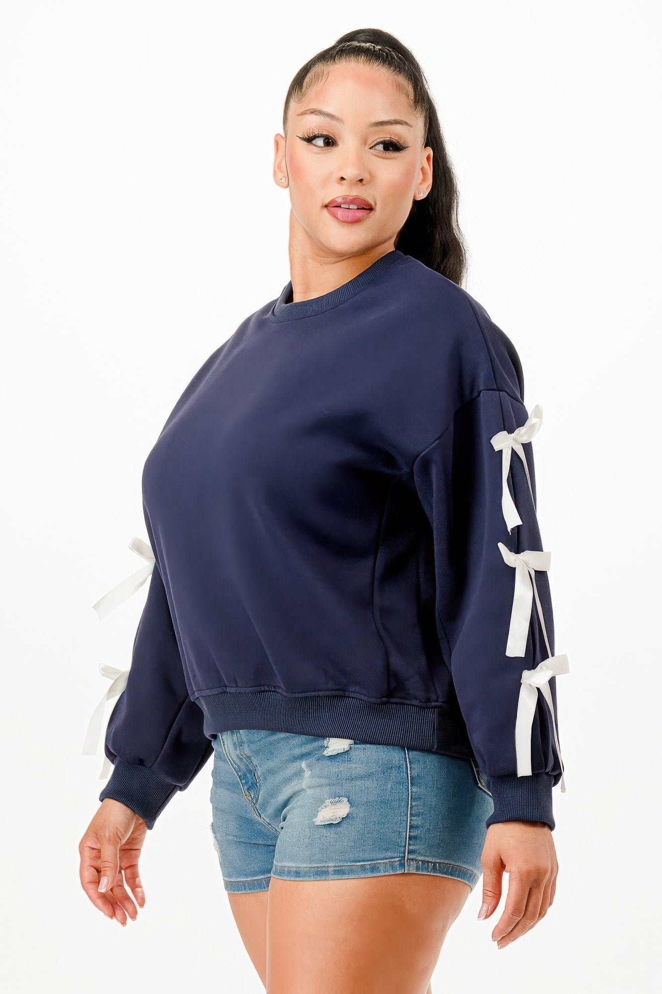 A woman wearing a navy blue crewneck sweatshirt with white bows on sleeves