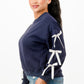 A woman wearing a navy blue crewneck sweatshirt with white bows on sleeves