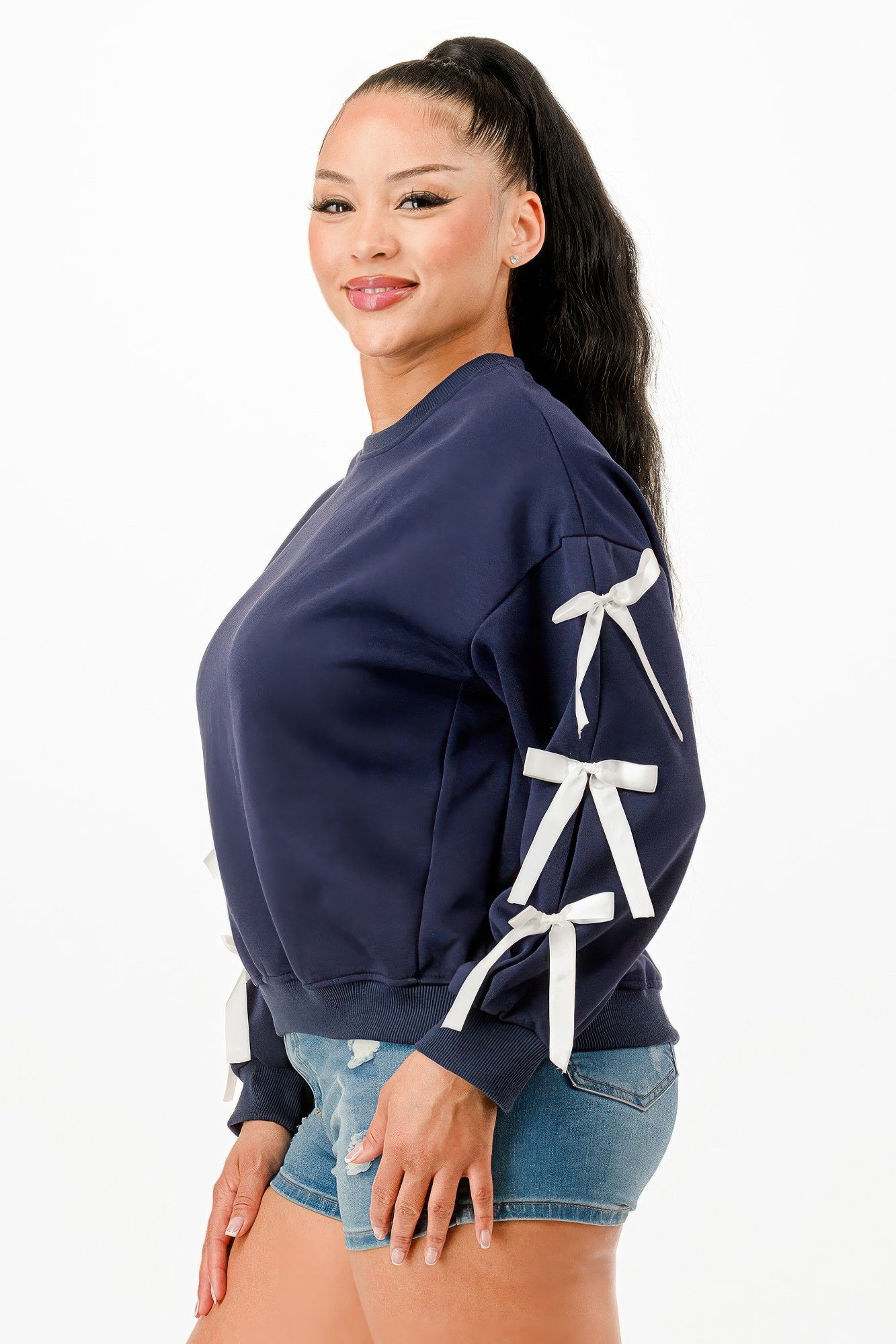 A woman wearing a navy blue crewneck sweatshirt with white bows on sleeves