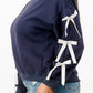 Side view of a woman wearing a navy blue crewneck sweatshirt with white bows on sleeves