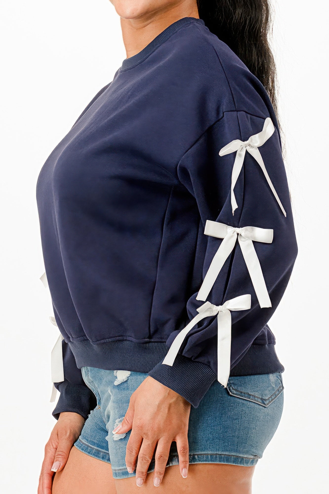 Side view of a woman wearing a navy blue crewneck sweatshirt with white bows on sleeves