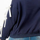 Back view of a woman wearing a navy blue crewneck sweatshirt with white bows on sleeves