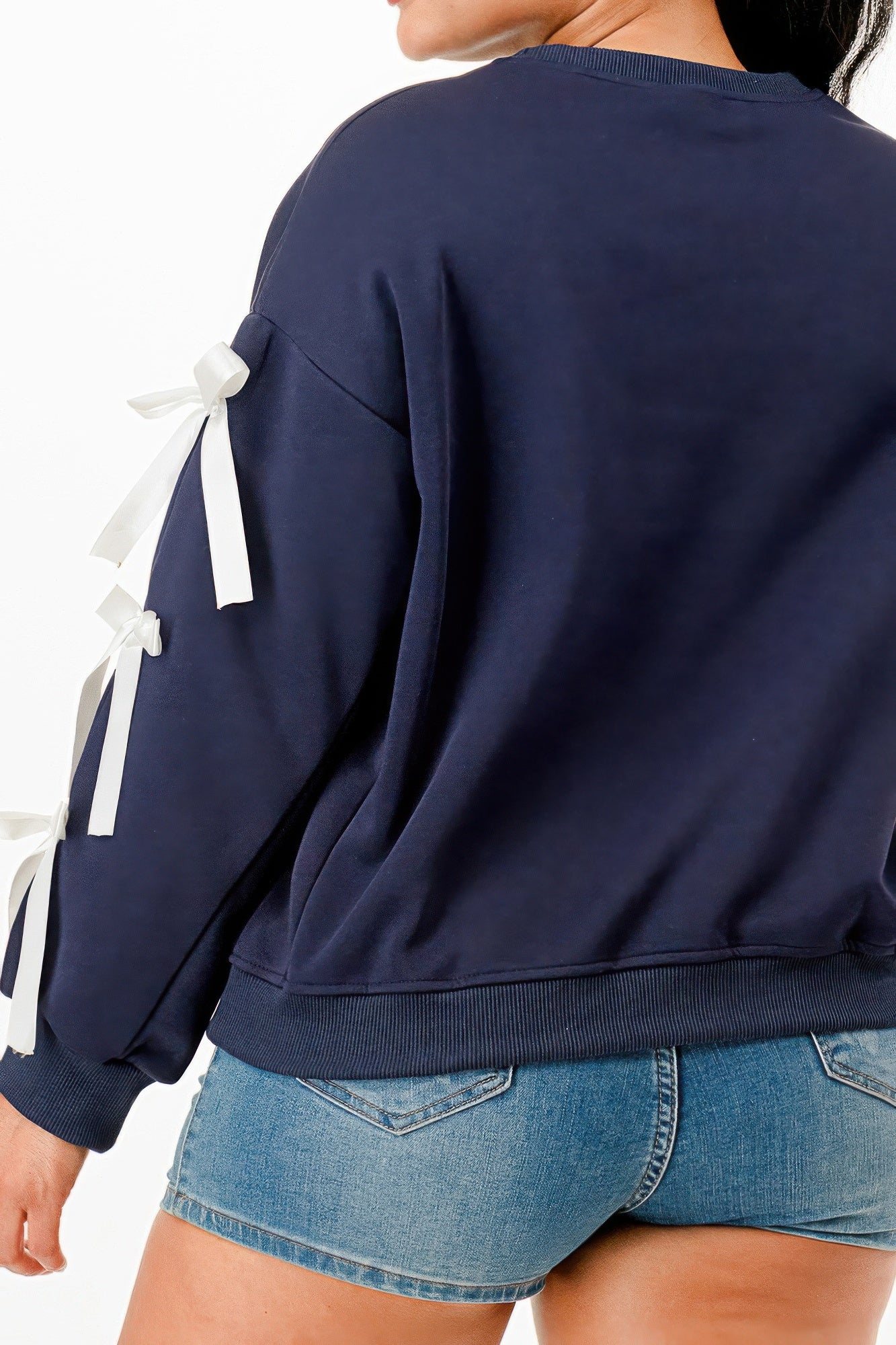 Back view of a woman wearing a navy blue crewneck sweatshirt with white bows on sleeves