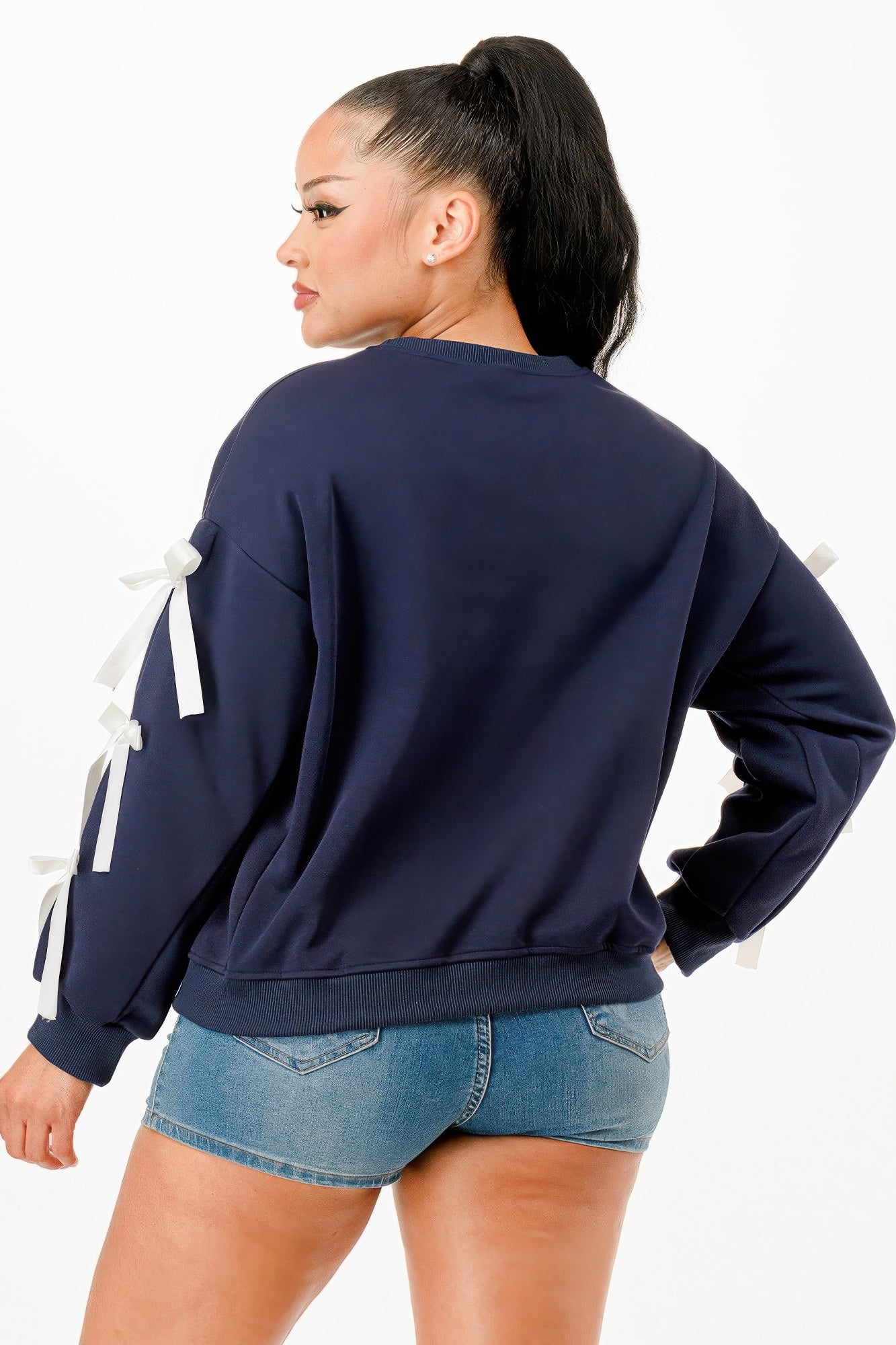 Back view of a woman wearing a navy blue crewneck sweatshirt with white bows on sleeves