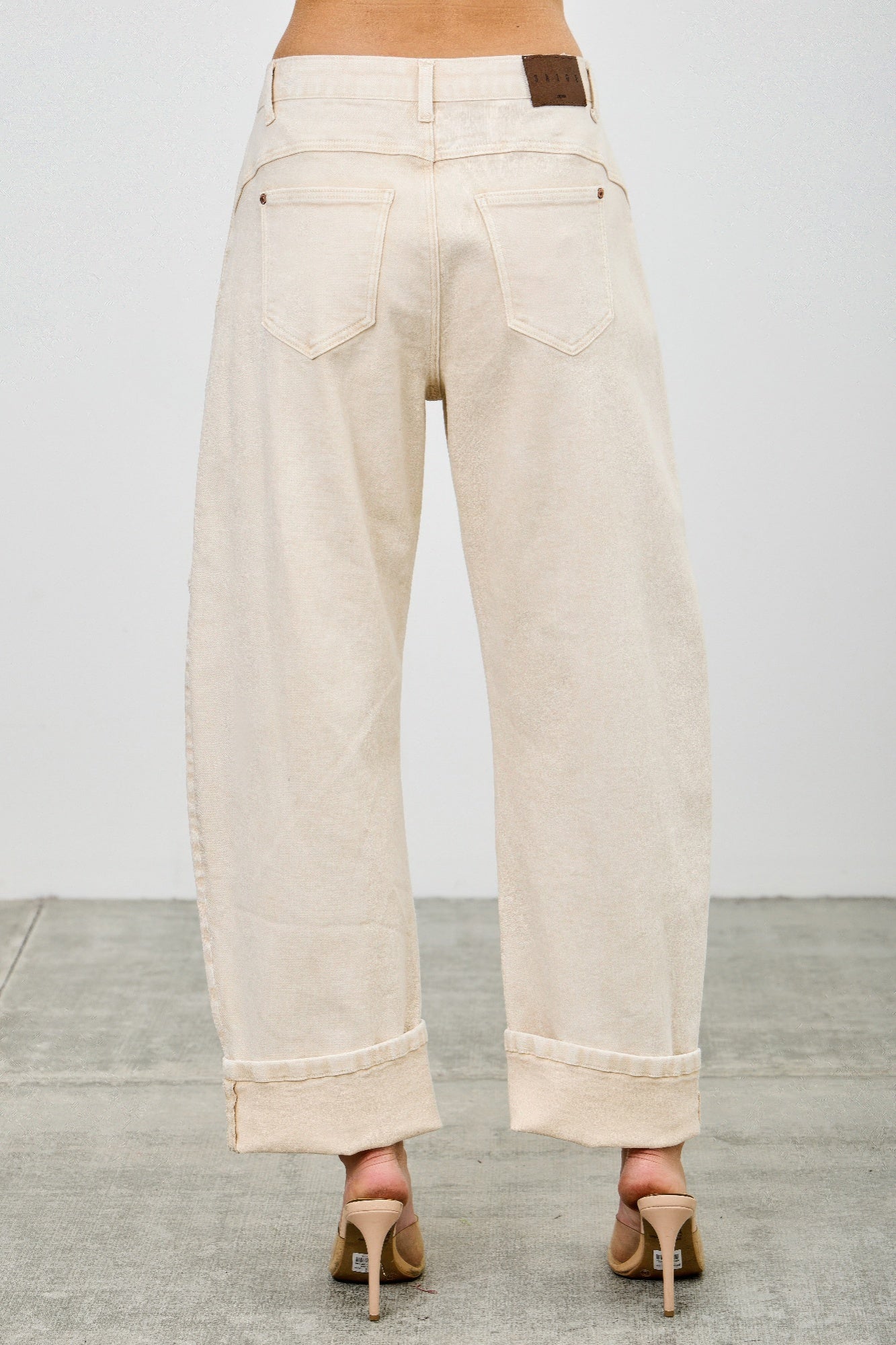 High-rise beige wide-leg denim pants with rolled cuffs and brown leather patch