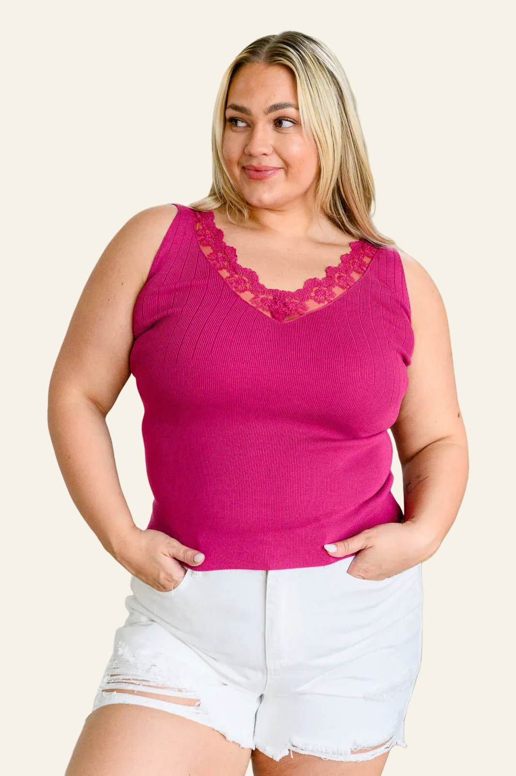 Woman wearing a pink tank top with lace details and white shorts on a beige background