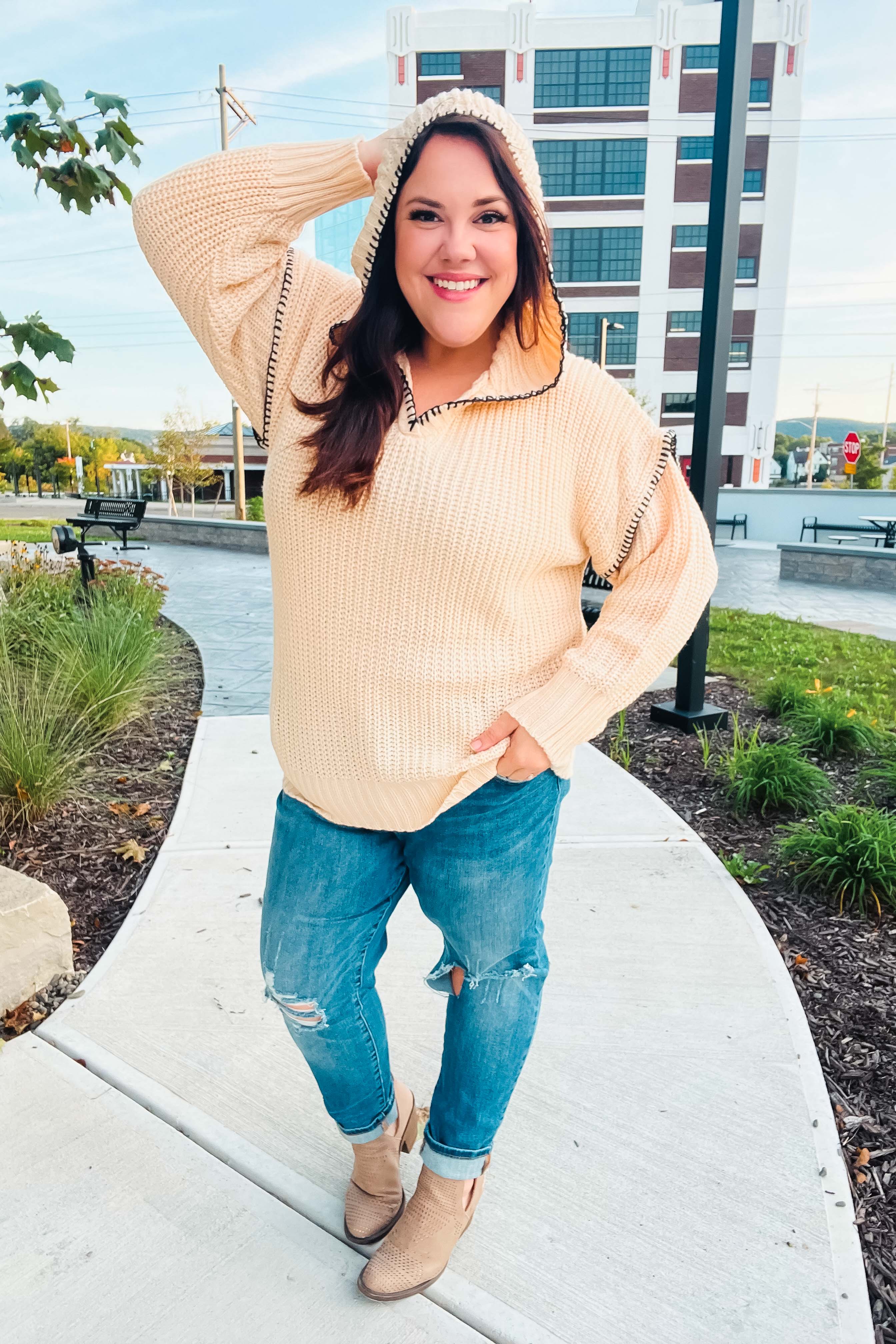 Cream-colored cable-knit hoodie with black-trimmed edges and notched neck