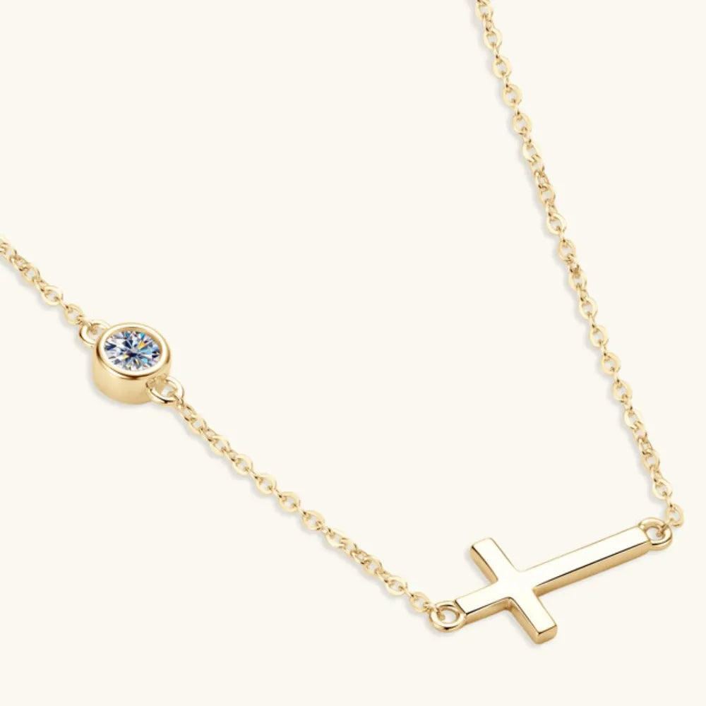 Gold necklace with a small round bezel moissanite stone and a cross-shaped pendant on a white background