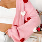Pink knitted open front cardigan with red and white heart pom-poms