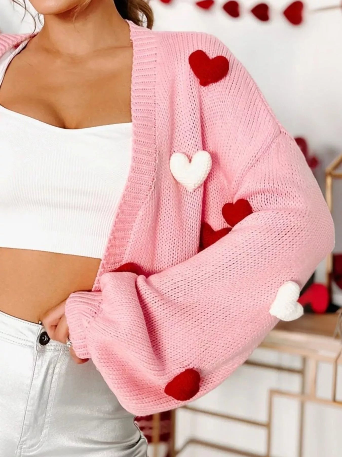 Pink knitted open front cardigan with red and white heart pom-poms