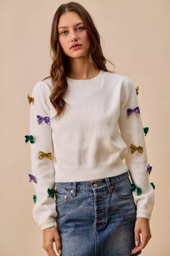 White knit sweater with colorful sequined bows in gold, purple, and green