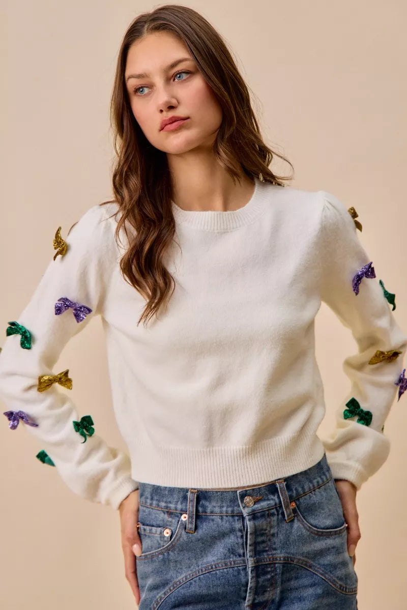 White knit sweater with colorful sequined bow embellishments on sleeves