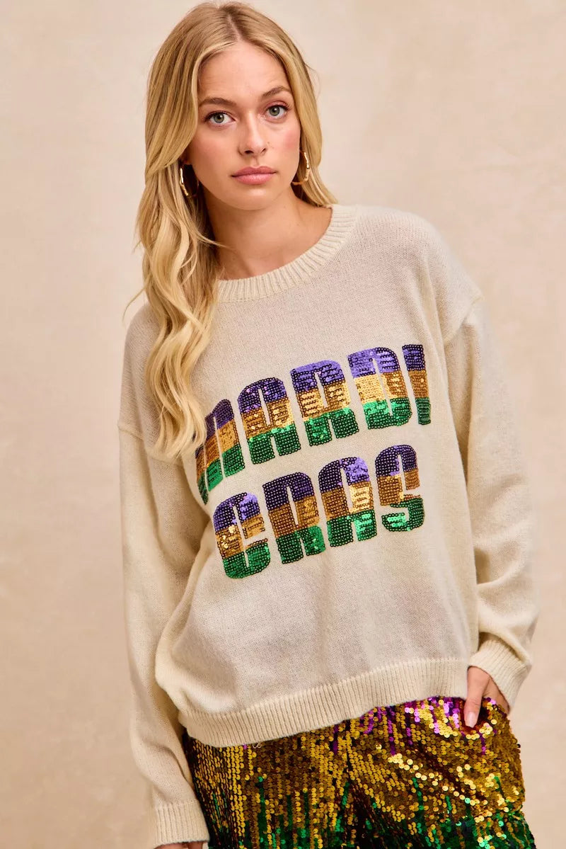 Cream-colored BiBi Mardi Gras sequin lettering knit top with vibrant purple, green, gold chest design