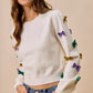 White knit sweater with purple, green, gold sequined bows and stars