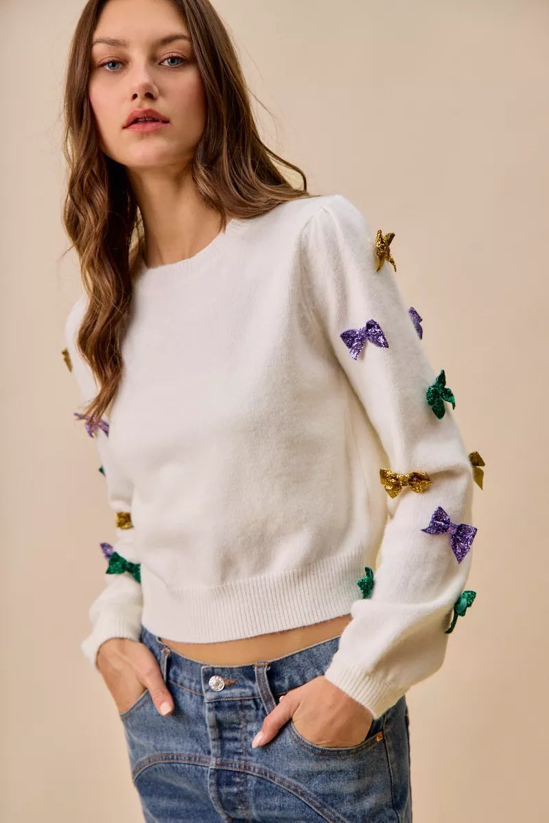 White knit sweater with purple, green, gold sequined bows and stars