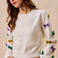 White knit sweater with colorful sequined bows in gold, purple, green