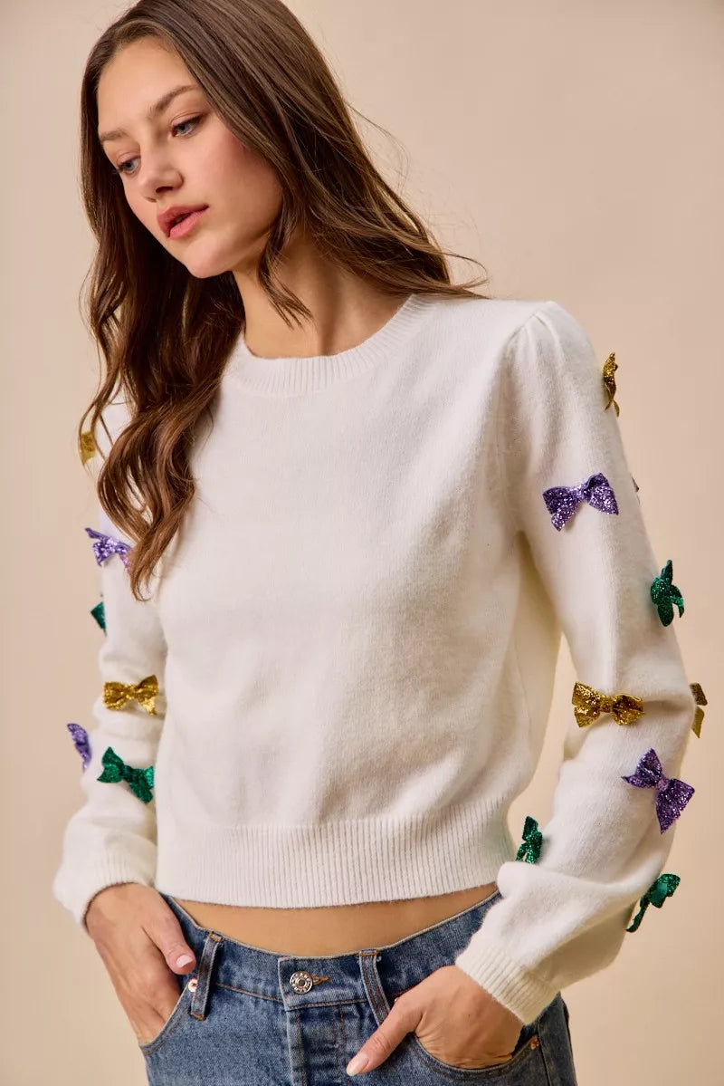 White knit sweater with colorful sequined bows in gold, purple, green