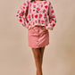 Pink sweater with red roses, hearts, and scalloped hem on denim skirt