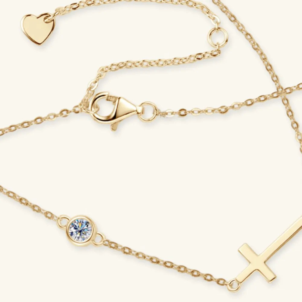 Gold horizontal cross necklace with round moissanite stone laying on a white table