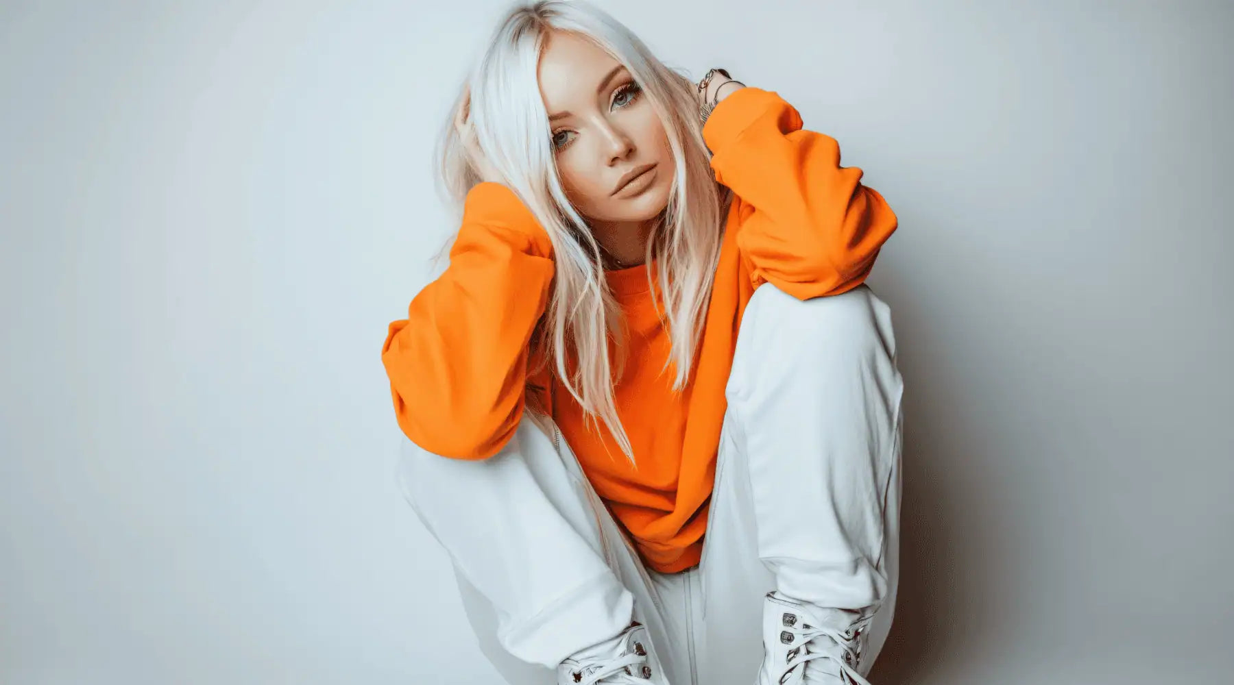 A woman wearing a orange sweatshirt and white pants on a plain background