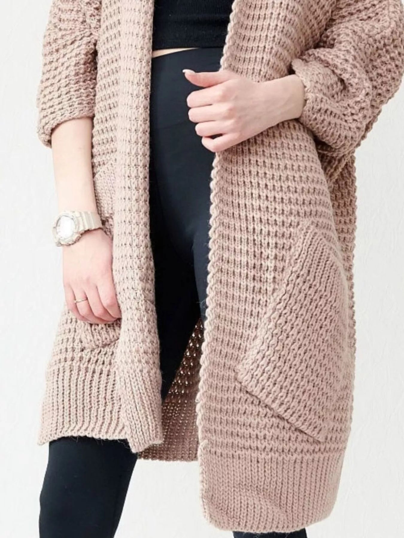Woman wearing a blush-pink Chunky Knit Open Front Cardigan with a textured waffle weave and deep front pockets, styled over a black top.
