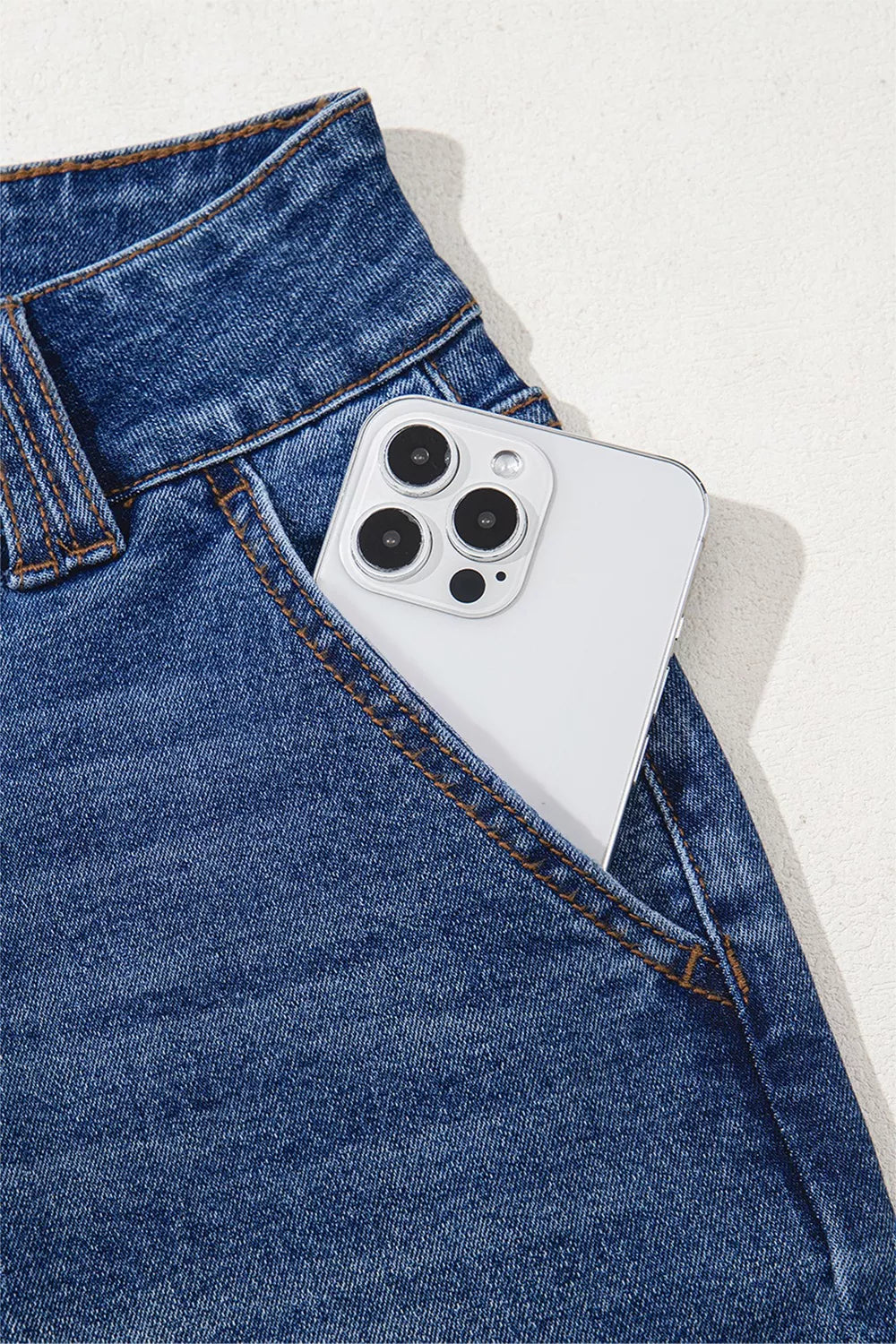 White iPhone with triple-lens camera in Daverri jeans pocket