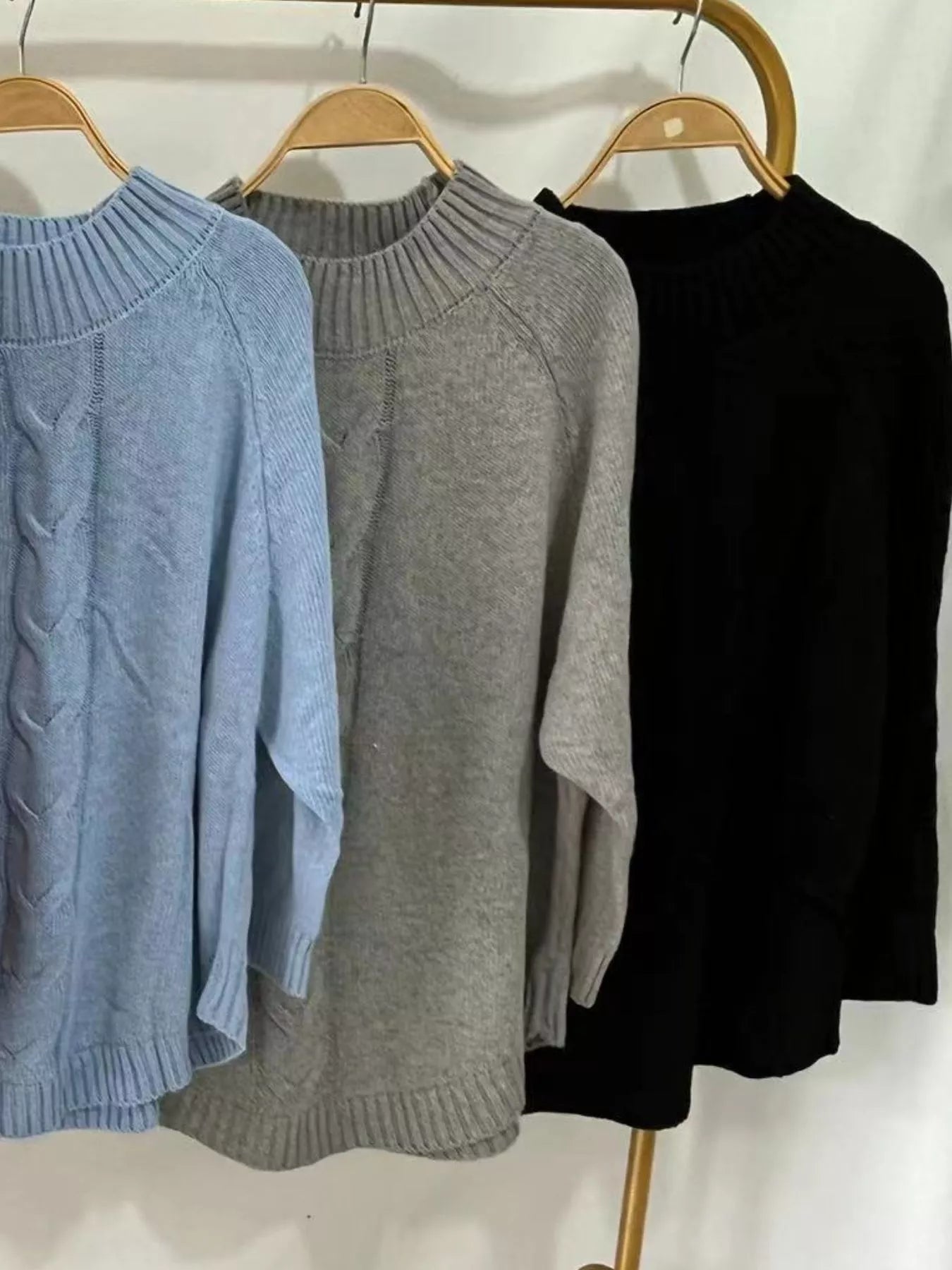 Three full-size cable-knit sweaters in blue, gray, black on hangers