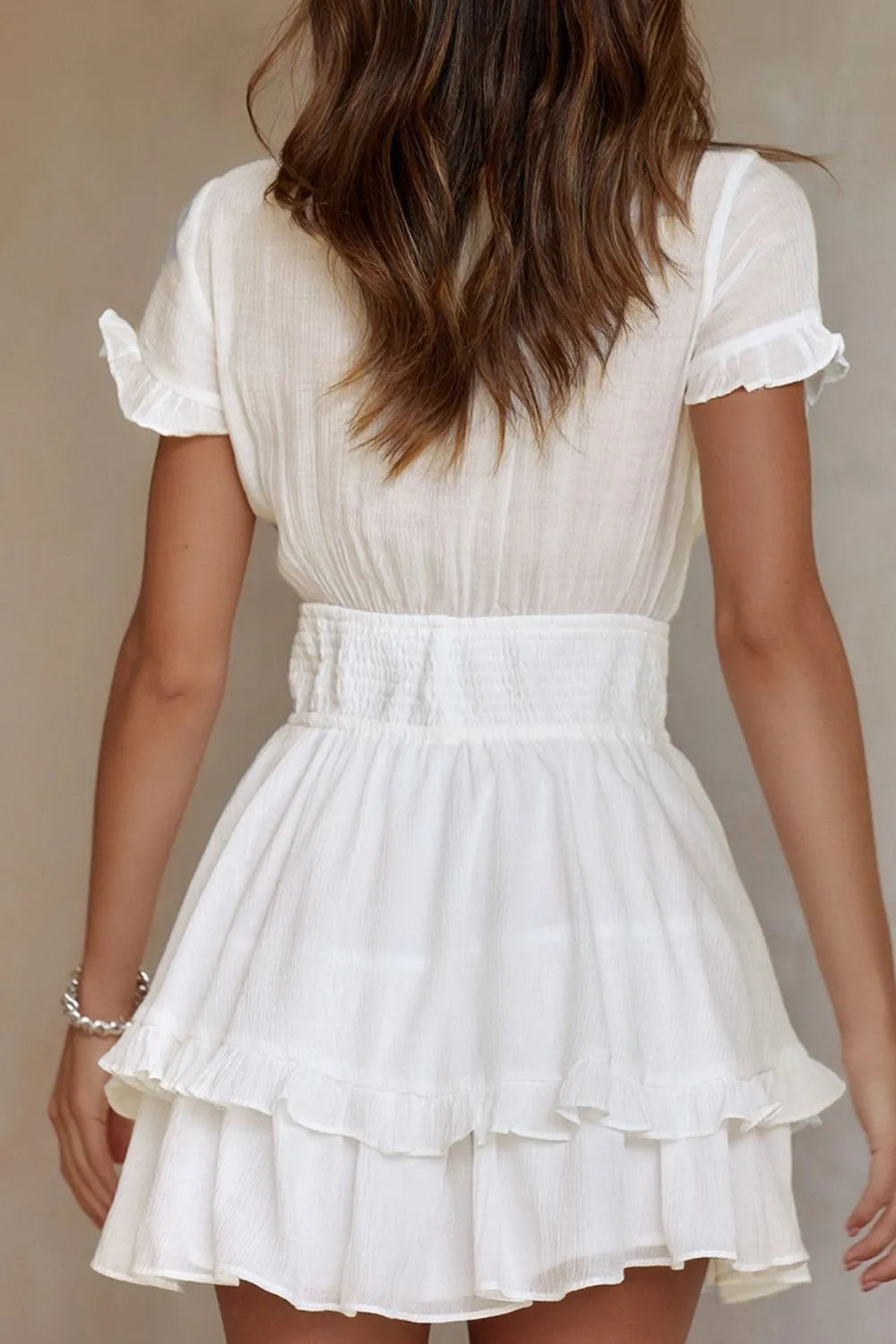 White tie-front mini dress with smocked waist, tiered ruffles, and flutter sleeves