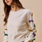 White SO ME Mardi Gras glitter bow knit sweater with sequined purple, green, gold bows on sleeves