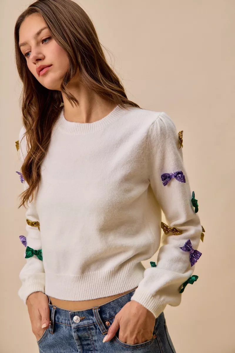 White SO ME Mardi Gras glitter bow knit sweater with sequined purple, green, gold bows on sleeves