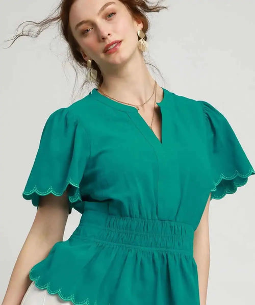 Woman wearing a teal blouse with scalloped edges on a plain background