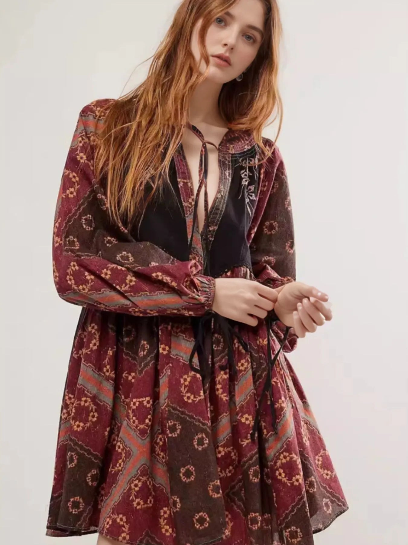 Woman in printed tie neck long sleeve boho mini dress with maroon brown motifs